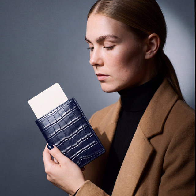 Woman holding a navy crocodile-embossed leather passport holder by GENTCREATE with a blank card tucked in