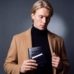 Man holding a matching navy crocodile-embossed leather passport holder and card holder set by GENTCREATE