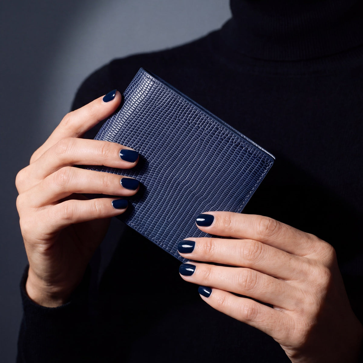 Close-up of hands holding a navy lizard-embossed leather bifold wallet by GENTCREATE