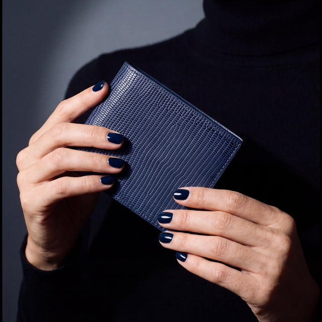 Close-up of hands holding a navy lizard leather bifold wallet by GENTCREATE