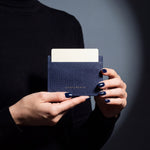 Close-up of hands holding a navy lizard-embossed leather card holder by GENTCREATE with a card in the top slot