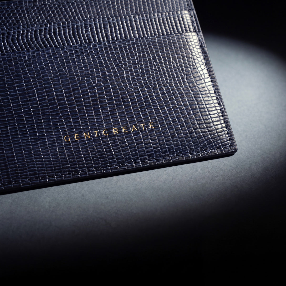 Close-up of the gold GENTCREATE stamp pressed into a navy lizard-embossed leather card holder