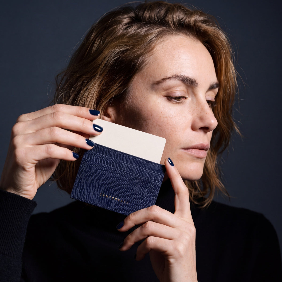 Woman holding a slim navy lizard-embossed leather card holder by GENTCREATE and drawing out a card