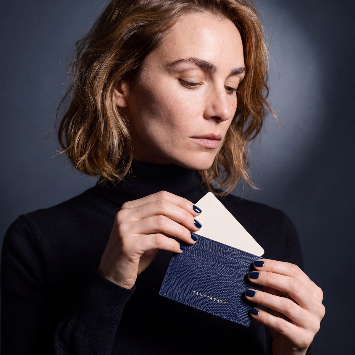 Woman sliding a card into a navy lizard-embossed leather card holder by GENTCREATE