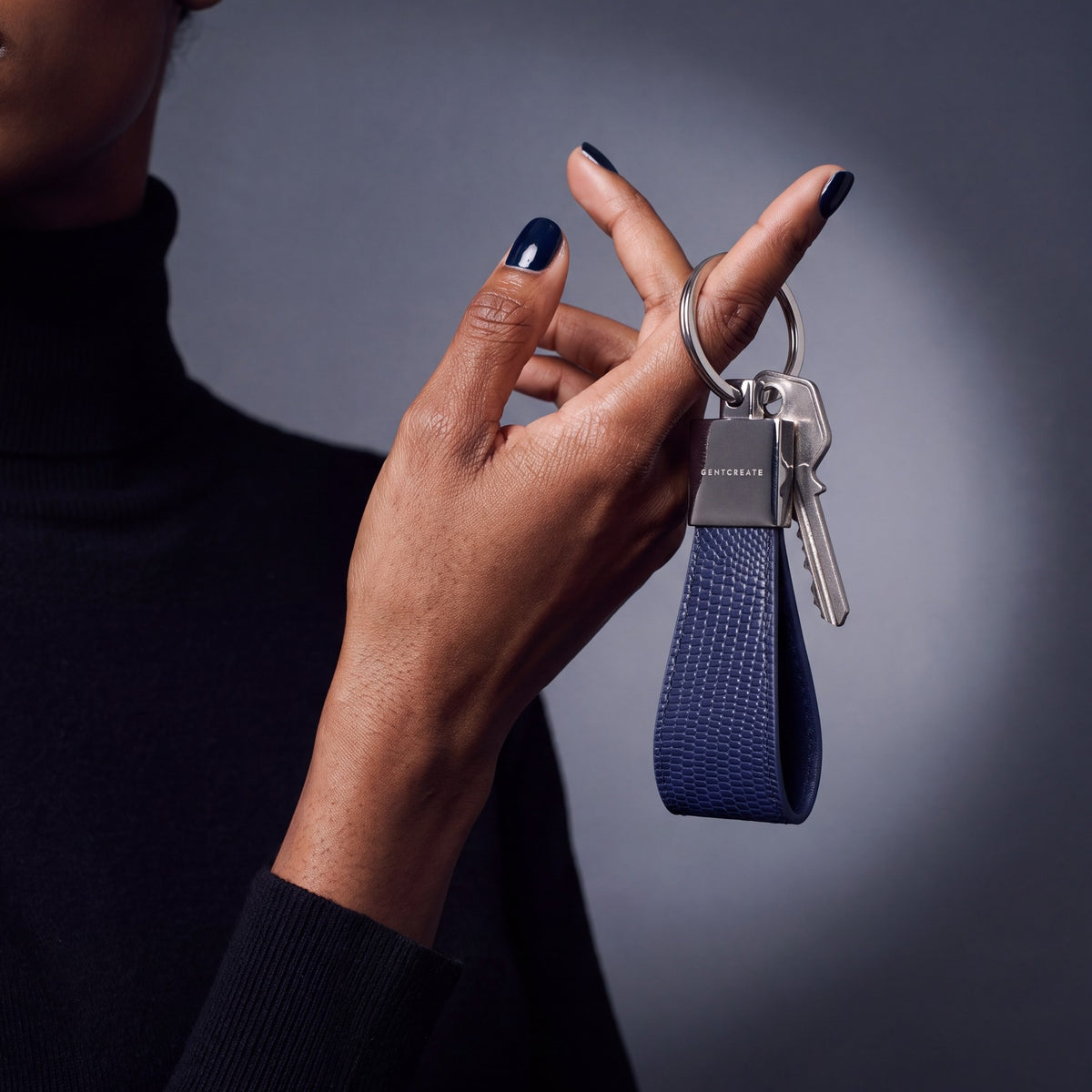 Close-up of a navy lizard-embossed leather keychain by GENTCREATE with house keys hanging from a finger
