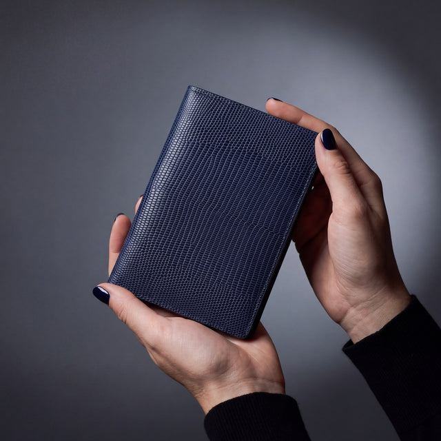 Close-up of hands holding a navy lizard leather passport holder by GENTCREATE