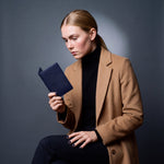 Woman seated, holding a navy lizard-embossed leather passport holder by GENTCREATE