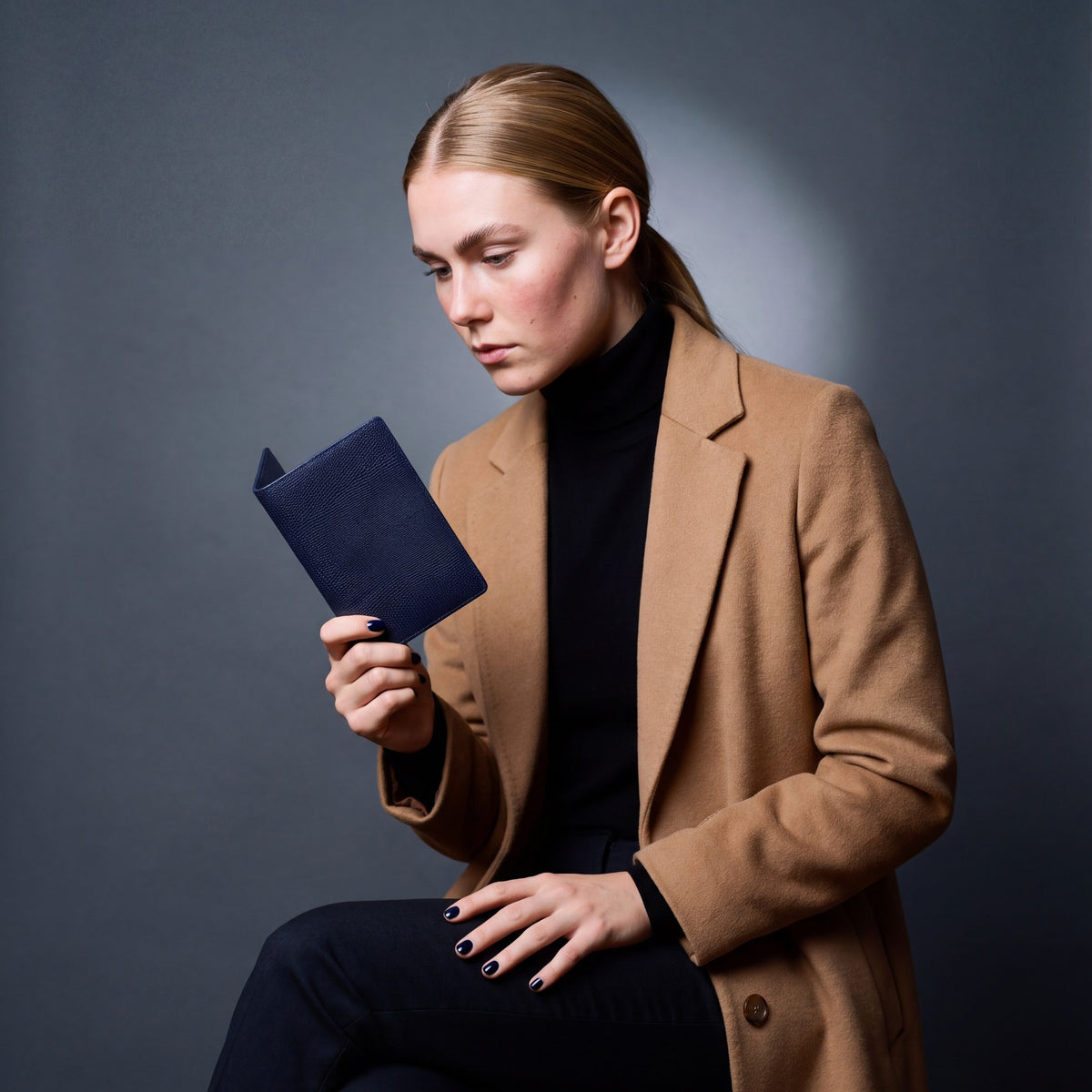 Woman seated, holding a navy lizard-embossed leather passport holder by GENTCREATE