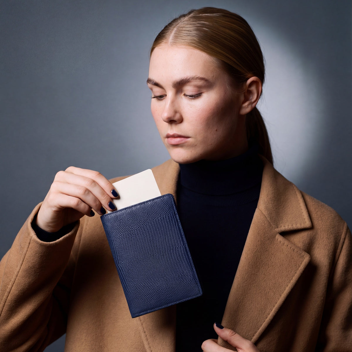 Woman holding a navy lizard-embossed leather passport holder by GENTCREATE with a blank card tucked in