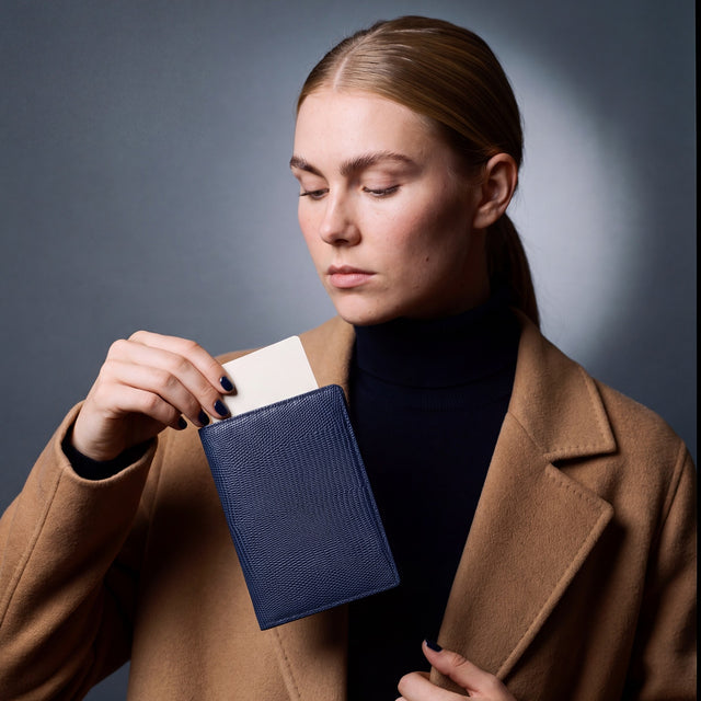 Woman holding a navy lizard leather passport holder by GENTCREATE with a blank card tucked in