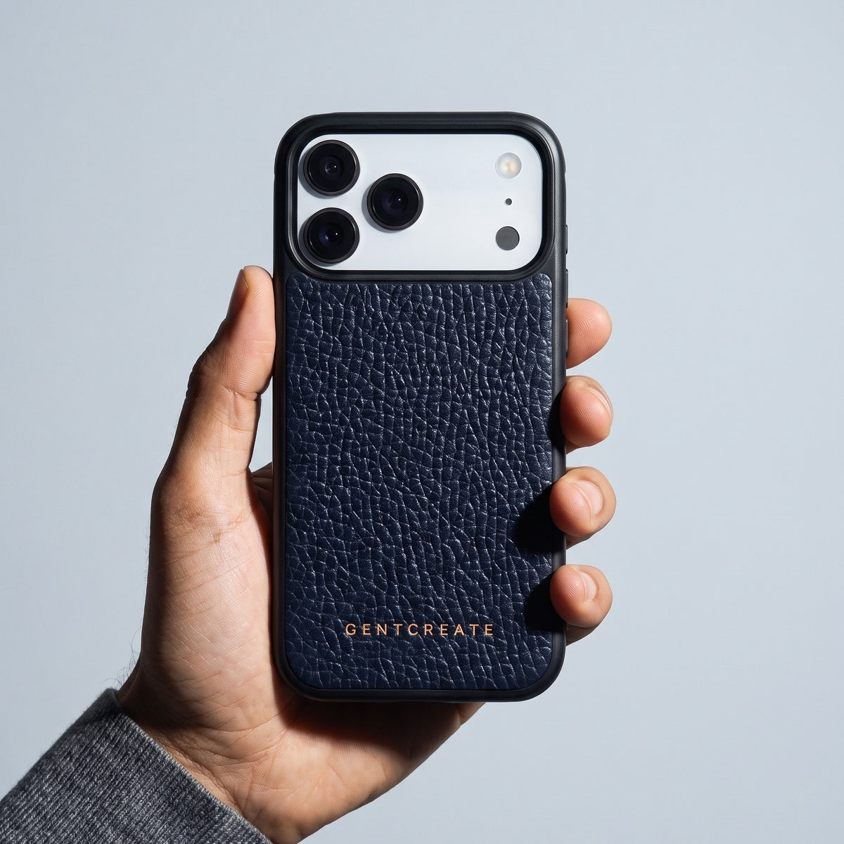 Hand holding a navy pebble-grain leather iPhone 18 Pro Max case by GENTCREATE against pale gray