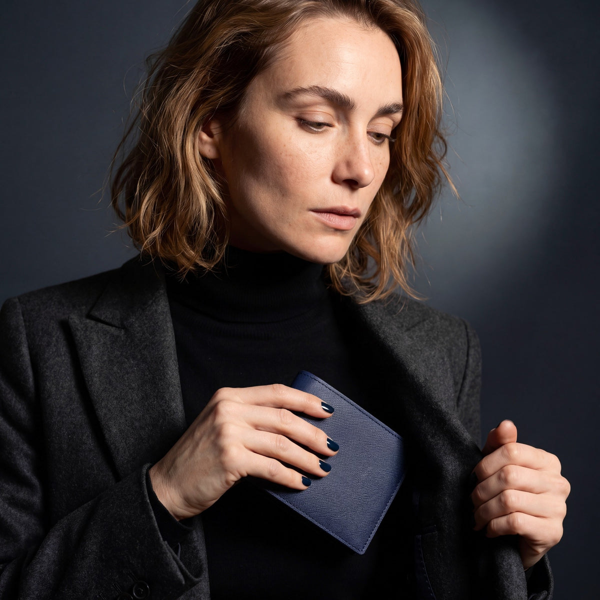 Woman in a blazer holding a navy Saffiano leather bifold wallet by GENTCREATE