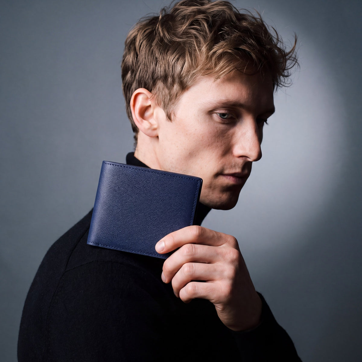 Man holding a navy Saffiano leather bifold wallet by GENTCREATE up over the shoulder