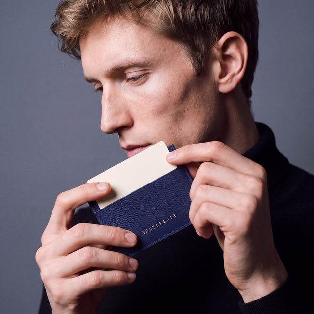 Man holding a slim navy Saffiano leather card holder by GENTCREATE and drawing out a card
