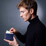 Man sliding a card into a navy Saffiano leather card holder by GENTCREATE