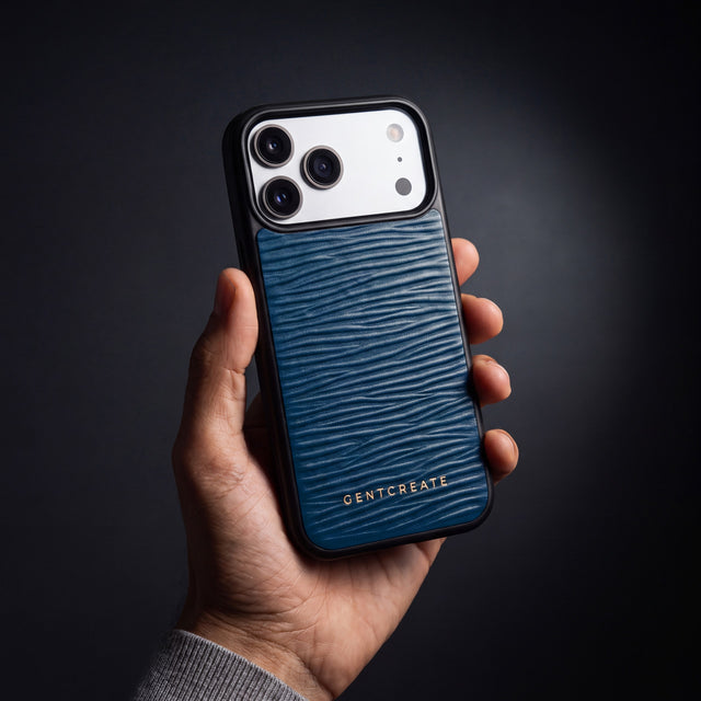 Mannshånd som holder et marineblått iPhone 18 Pro Max-deksel i bølgepreget kalveskinn fra GENTCREATE i et mørkt studio