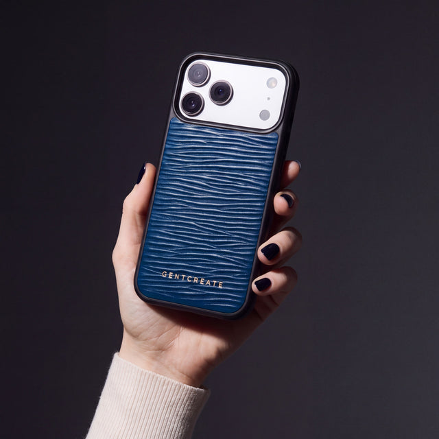 Hånd med marineblå negler som holder et marineblått iPhone 18 Pro Max-deksel i bølgepreget kalveskinn fra GENTCREATE