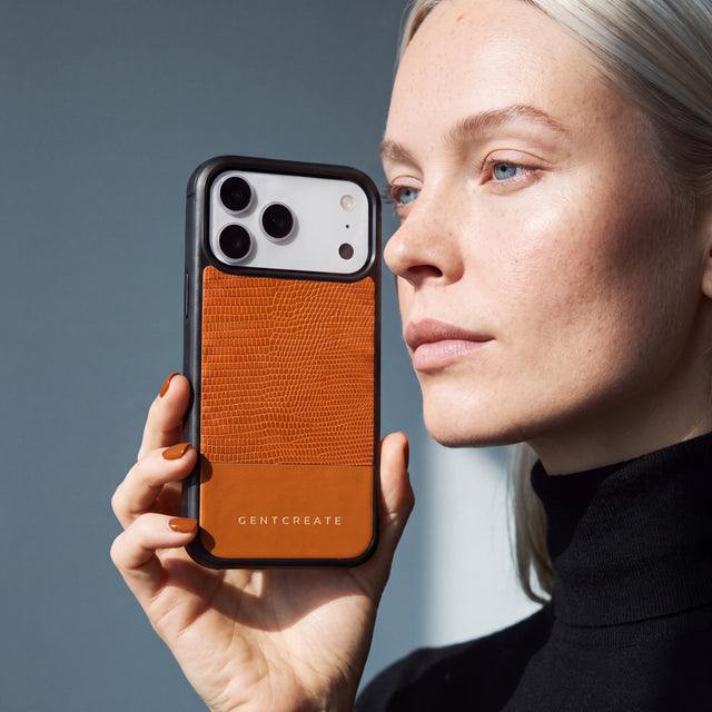 امرأة تمسك جرابًا برتقاليًا لهاتف iPhone 18 Pro Max من جلد عجل بنقش السحلية البارز من GENTCREATE بجانب وجهها تحت ضوء النافذة
