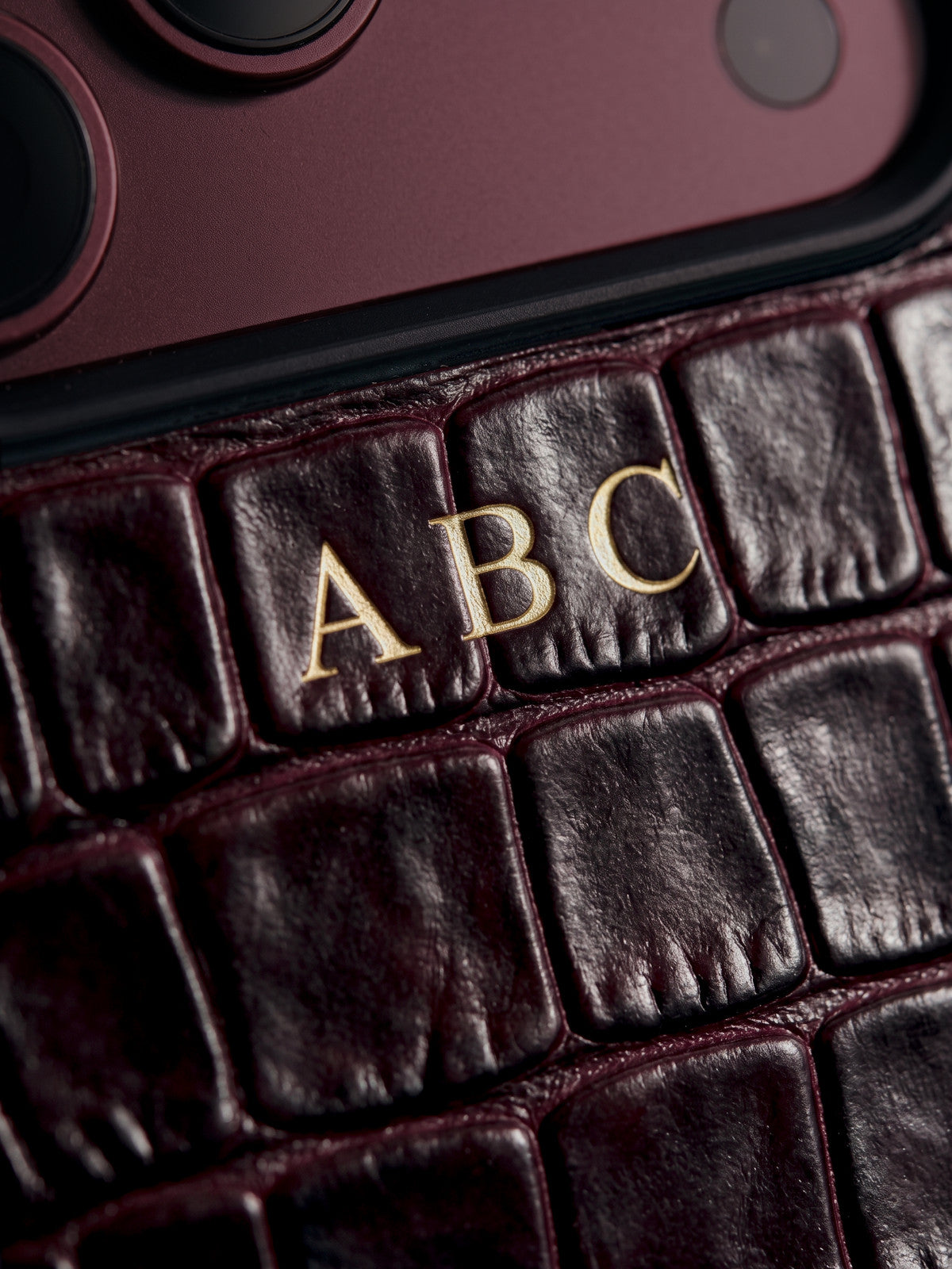Visualization: close-up of the burgundy croco-embossed case on day 1, with the initials ABC hot-stamped by hand in 24-karat gold foil.