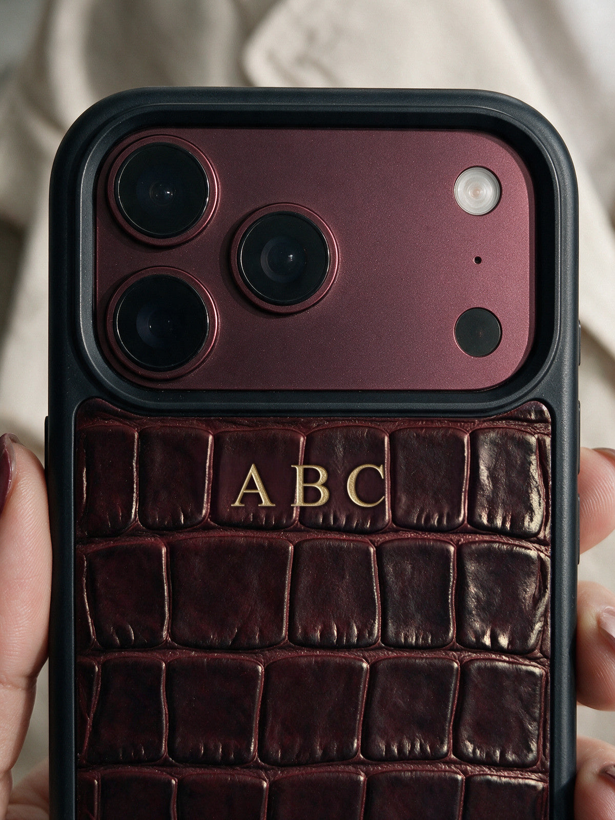 Visualization: the same personalized case after a year of daily use, with a natural patina. The burgundy is about 6% deeper and richer, the edges and corners are darker where the hand holds it, the raised scales have a soft burnish and the gloss has mellowed into a satin sheen. The gold foil initials ABC are intact.
