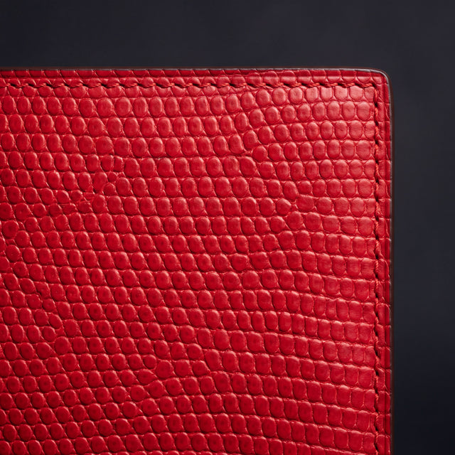 Close-up of the lizard-embossed grain and stitched corner of a red leather bifold wallet by GENTCREATE