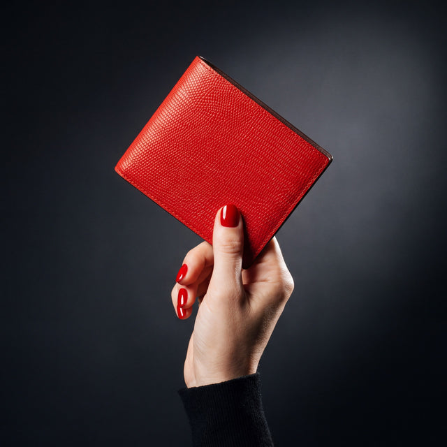 Woman's hand holding a red lizard-embossed leather bifold wallet by GENTCREATE in a dark studio