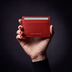 Woman's hand holding a red lizard-embossed leather business card holder by GENTCREATE in a dark studio