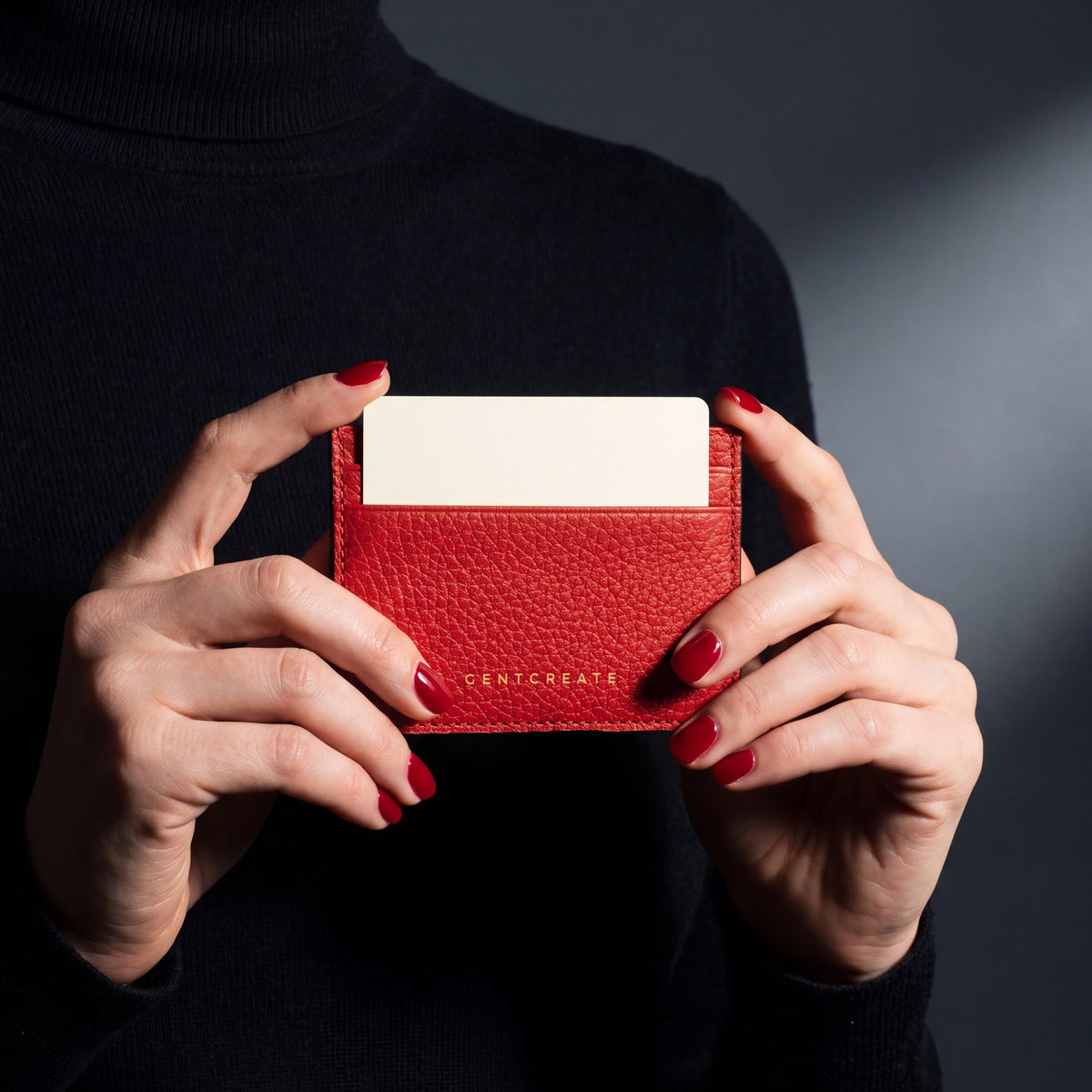 Close-up of hands holding a red pebble leather card holder by GENTCREATE with a card in the top slot