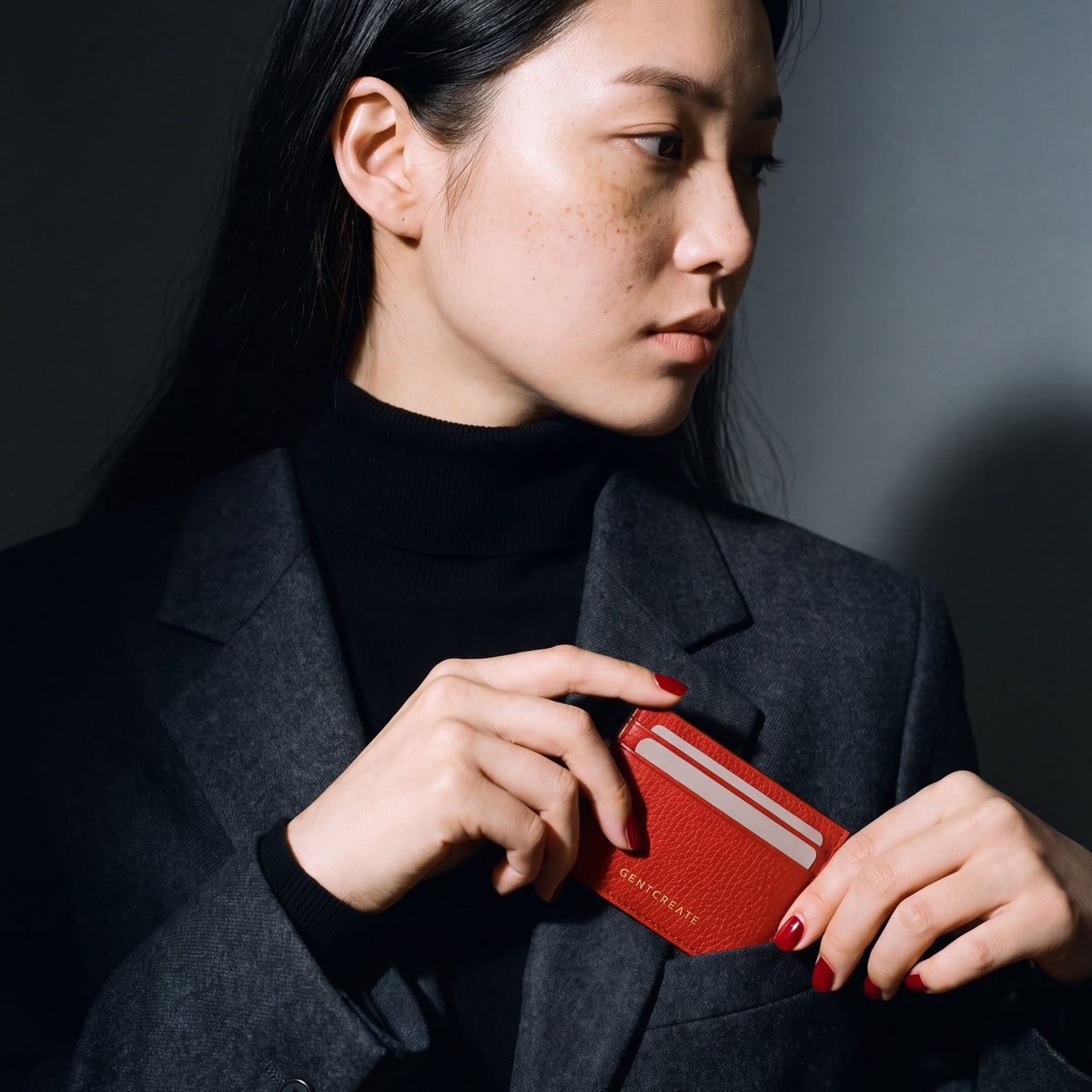 Woman slipping a red pebble leather card holder by GENTCREATE into a blazer chest pocket