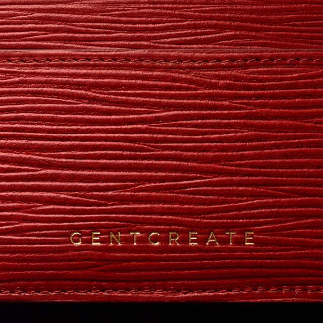 Κοντινό πλάνο της χρυσής σφραγίδας GENTCREATE σε κόκκινη καρτοθήκη από δέρμα με κυματιστό ανάγλυφο