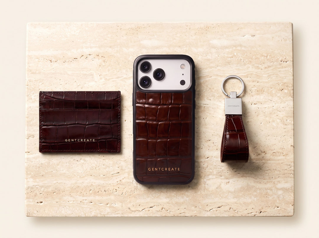 A brown crocodile-embossed GENTCREATE card holder, iPhone case and keychain laid out on stone