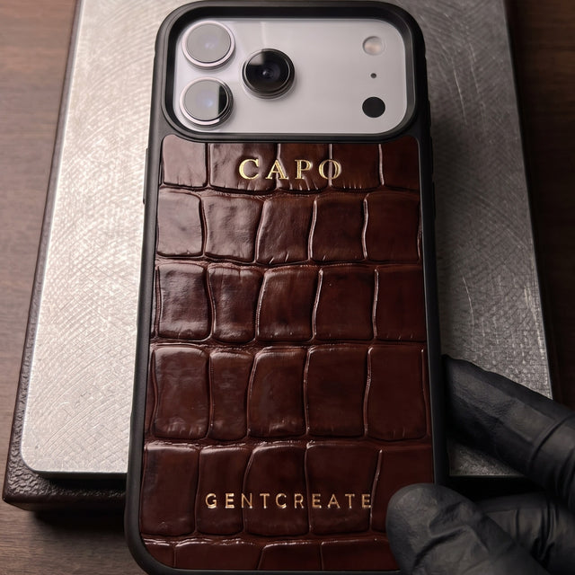 Brown croco-embossed leather iPhone case freshly hot-stamped with CAPO in gold, on the bed of a hot-foil press