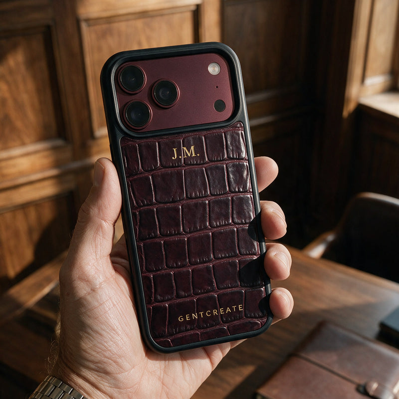 A man holds a burgundy croco-embossed leather iPhone case with his initials hot-stamped in gold, in a wood-paneled study