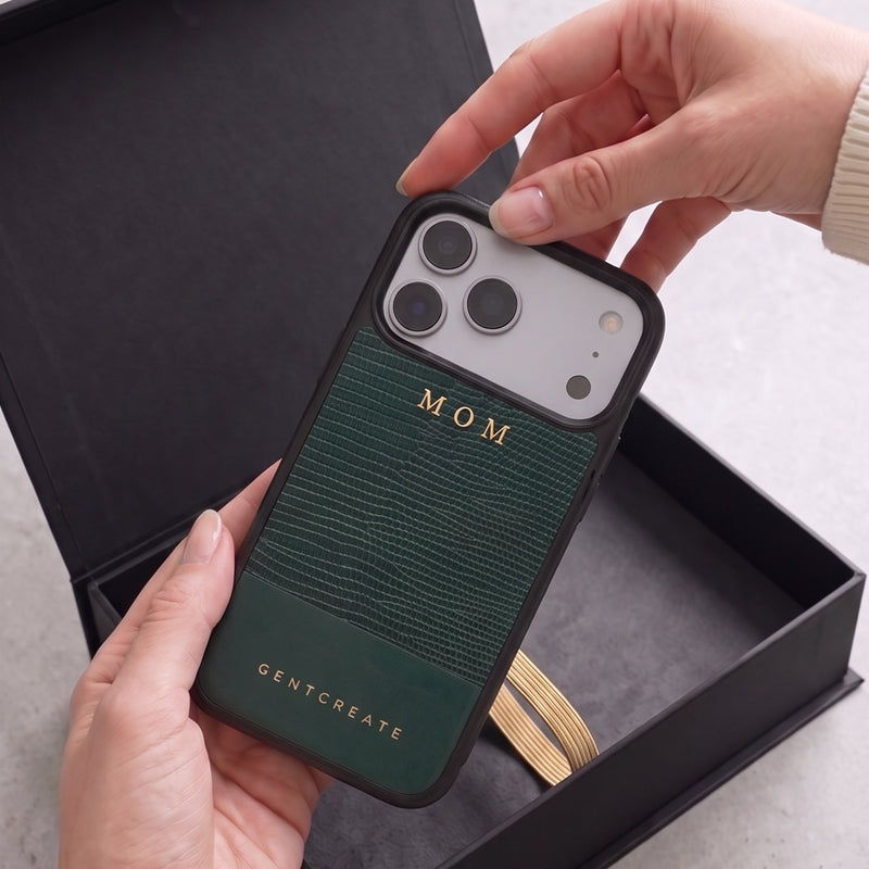 A woman lifts a green lizard-embossed leather iPhone case hot-stamped with MOM in gold out of an open GENTCREATE box
