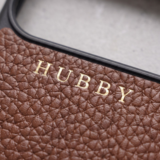 Close-up of HUBBY hot-stamped in gold foil on brown pebble-grain leather, just below the camera opening