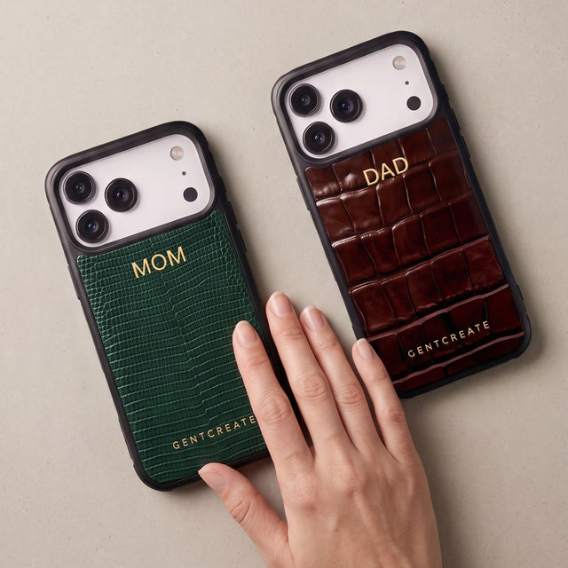 Green lizard-embossed and brown croco-embossed leather iPhone cases with MOM and DAD hot-stamped in gold, on warm stone with a woman's hand