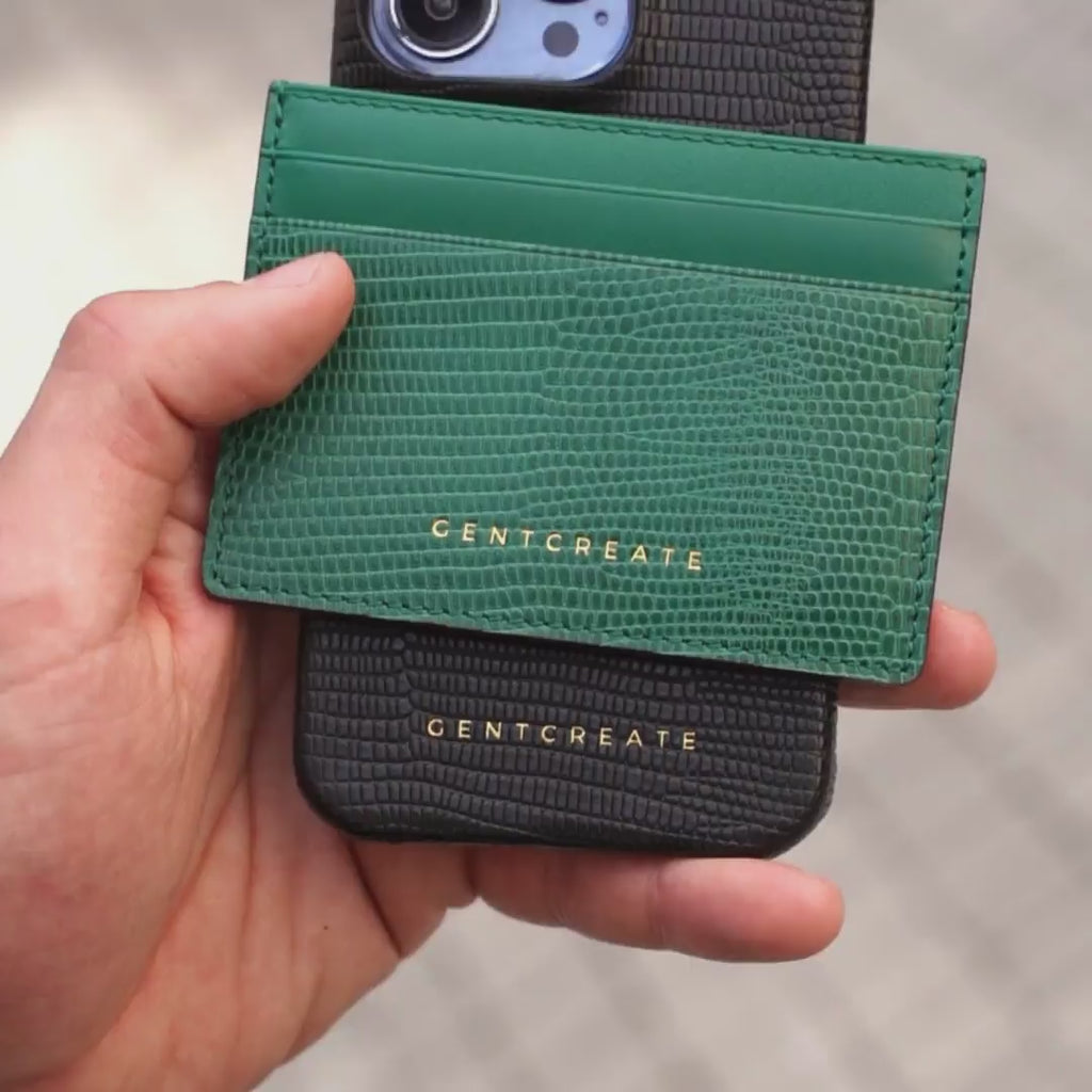 A man is holding a green lizard cardholder and a black lizard iPhone 15 Pro Max case.